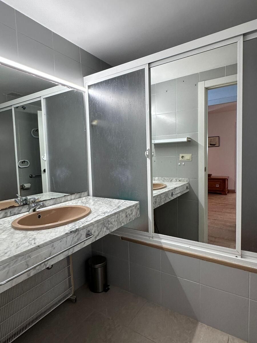 Baño con paredes grises, tocador de mármol, lavabo marrón, espejo y puerta abierta a una habitación.