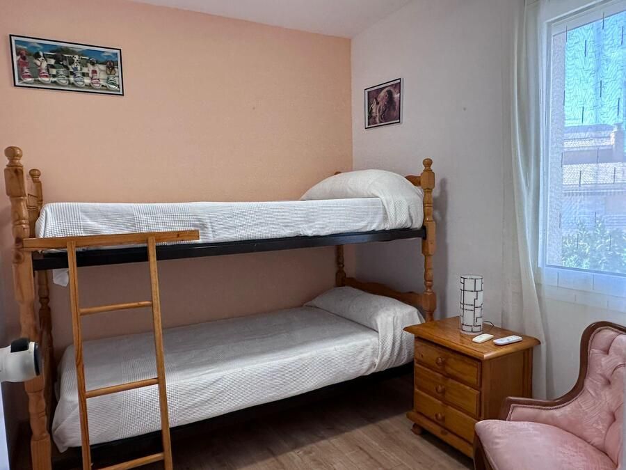 Literas en un dormitorio con pared rosa, muebles de madera y una ventana con cortina.