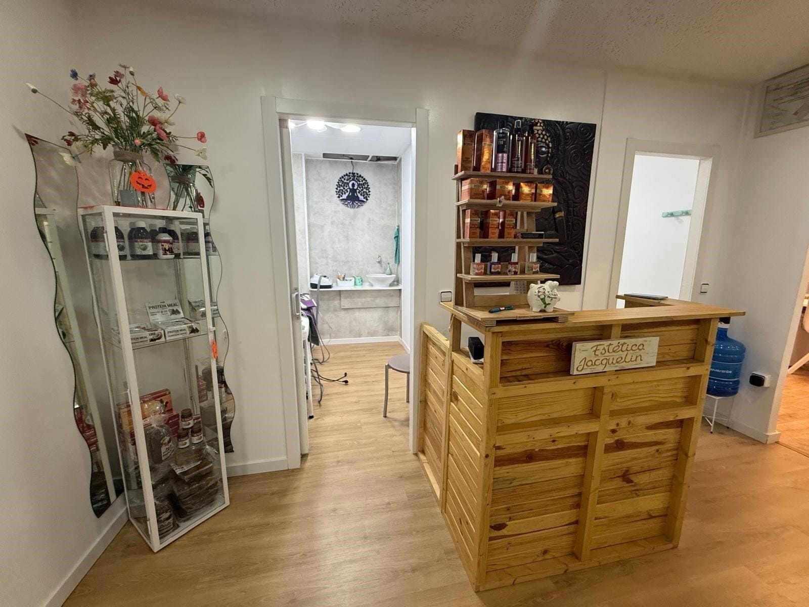 Mostrador de recepción de madera en la entrada de un salón. Estantes con productos, vitrina con flores y una puerta.