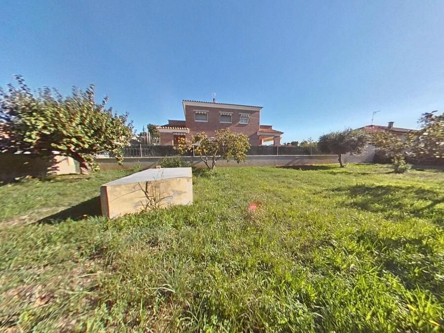 Un patio soleado y cubierto de césped con una casa de ladrillo de dos pisos al fondo, bajo un cielo azul claro.