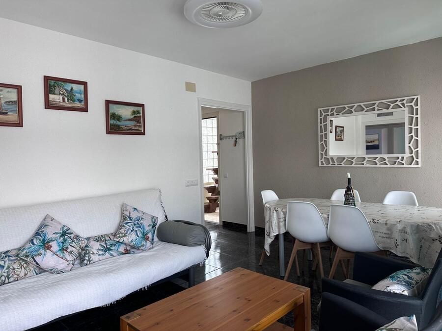 Sala de estar con sofá blanco, mesa de comedor, obras de arte enmarcadas y puerta que conduce a otra habitación.
