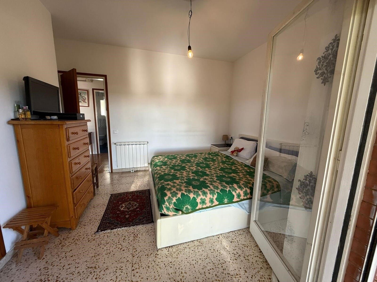 Dormitorio con cómoda, cama y armario con espejo. Entra la luz del sol.