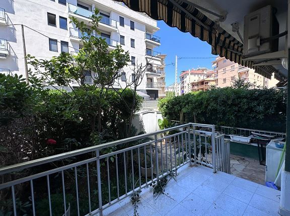 Un balcón con toldo a rayas está rodeado de árboles y edificios.