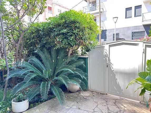 Un jardín con una puerta, plantas y árboles delante de un edificio.