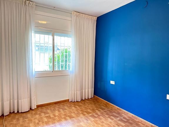 Una habitación vacía con una pared azul y cortinas blancas.