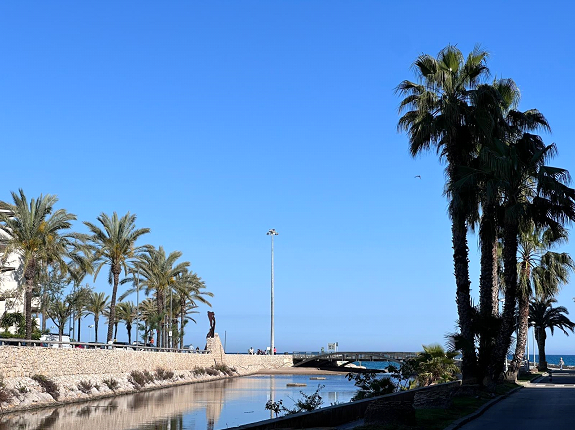 Una estatua de un hombre parado junto a un cuerpo de agua rodeado de palmeras.