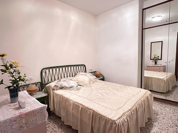 Un dormitorio con cama, mesita de noche, espejo y tocador.