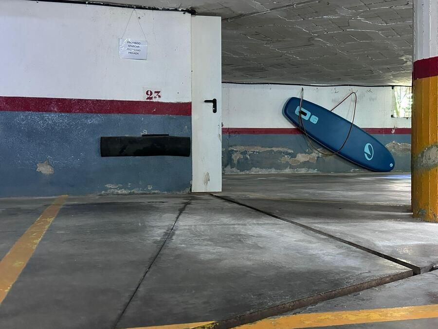 Interior de un aparcamiento. Tabla de surf azul colgada en la pared. Acentos rojos y amarillos en paredes y pilares.