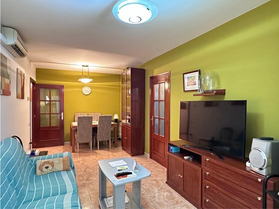 Sala de estar con sofá, TV, comedor y paredes verdes.