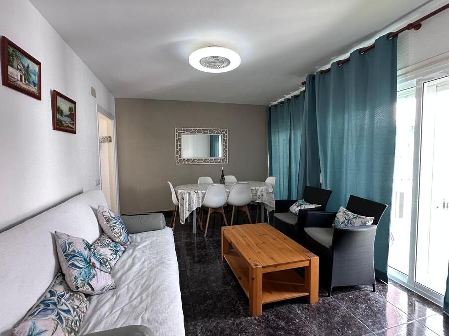 Sala de estar con sofá blanco, mesa de comedor, cortinas azules y suelo oscuro.