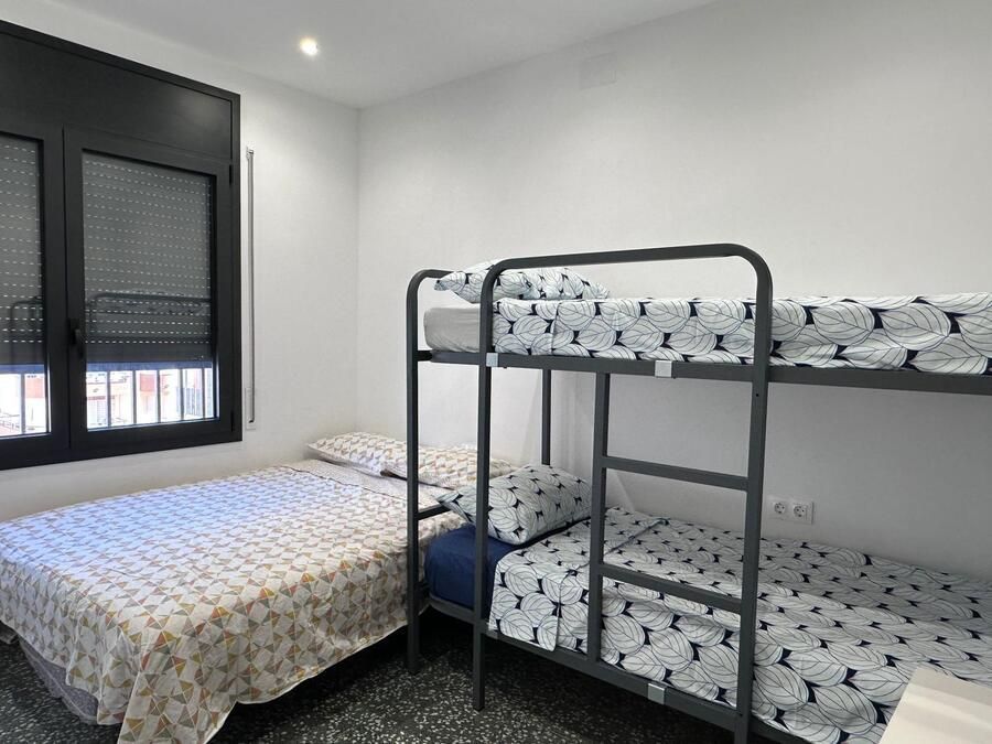 Dormitorio con una cama individual y una litera con ropa de cama estampada a juego, una ventana a la izquierda.