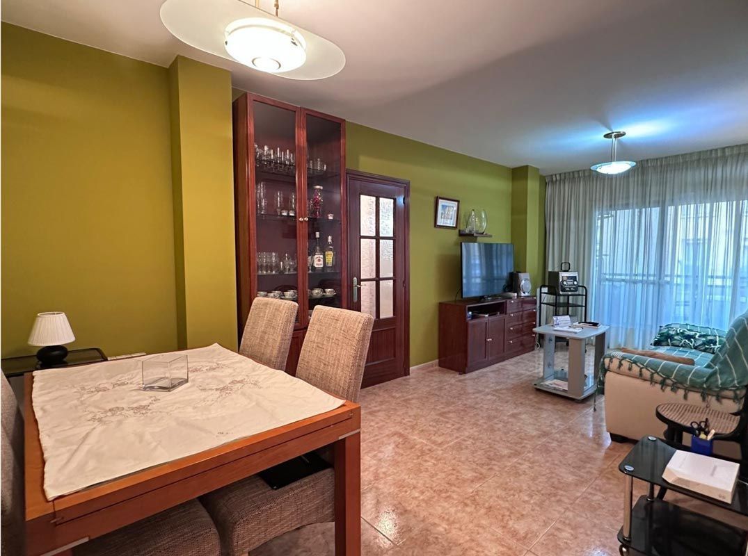 Sala de estar con mesa de comedor, vitrina, TV, sofá y paredes verdes.