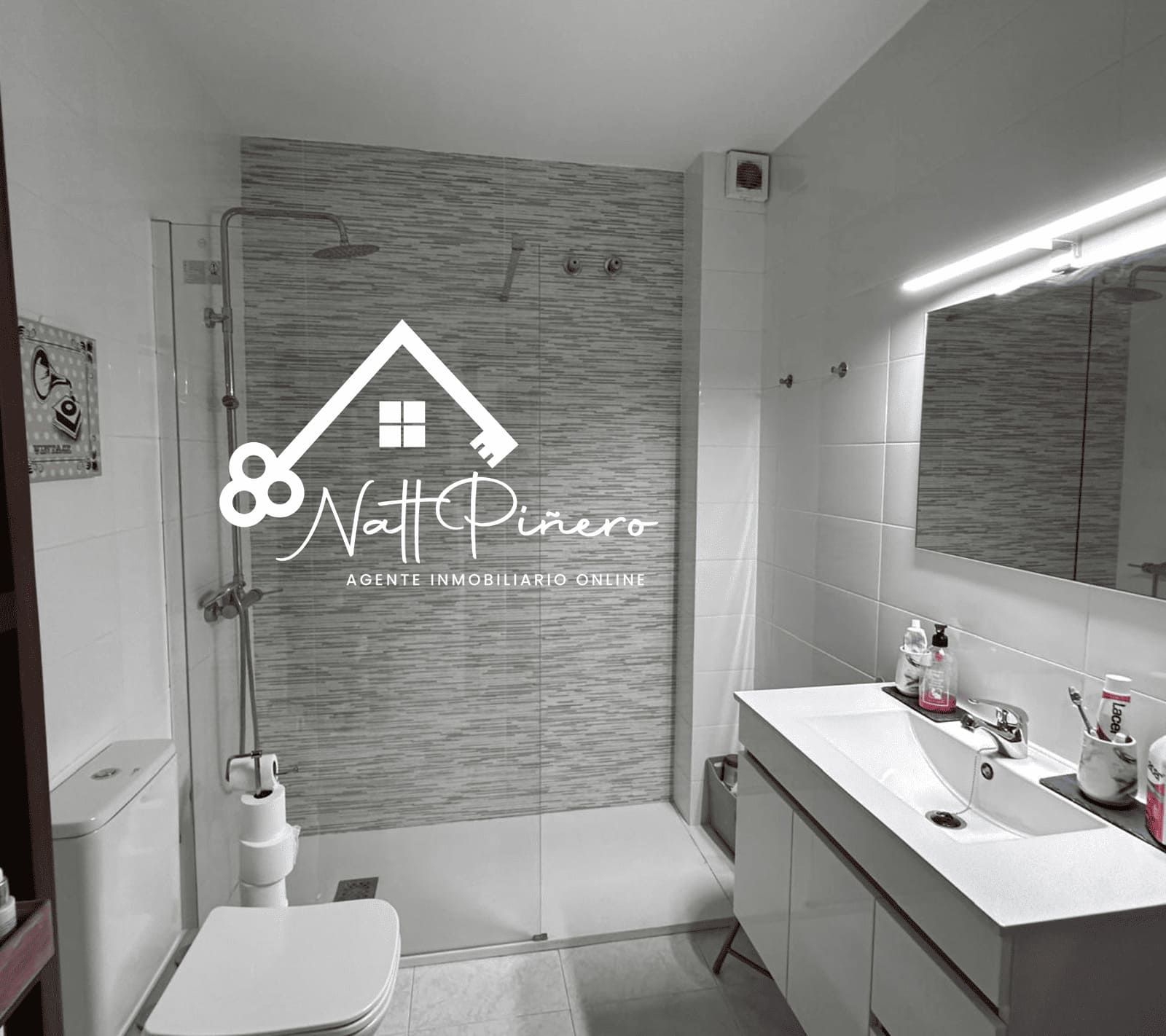 Baño con ducha, lavabo, inodoro y logotipo superpuesto. Blanco y negro.