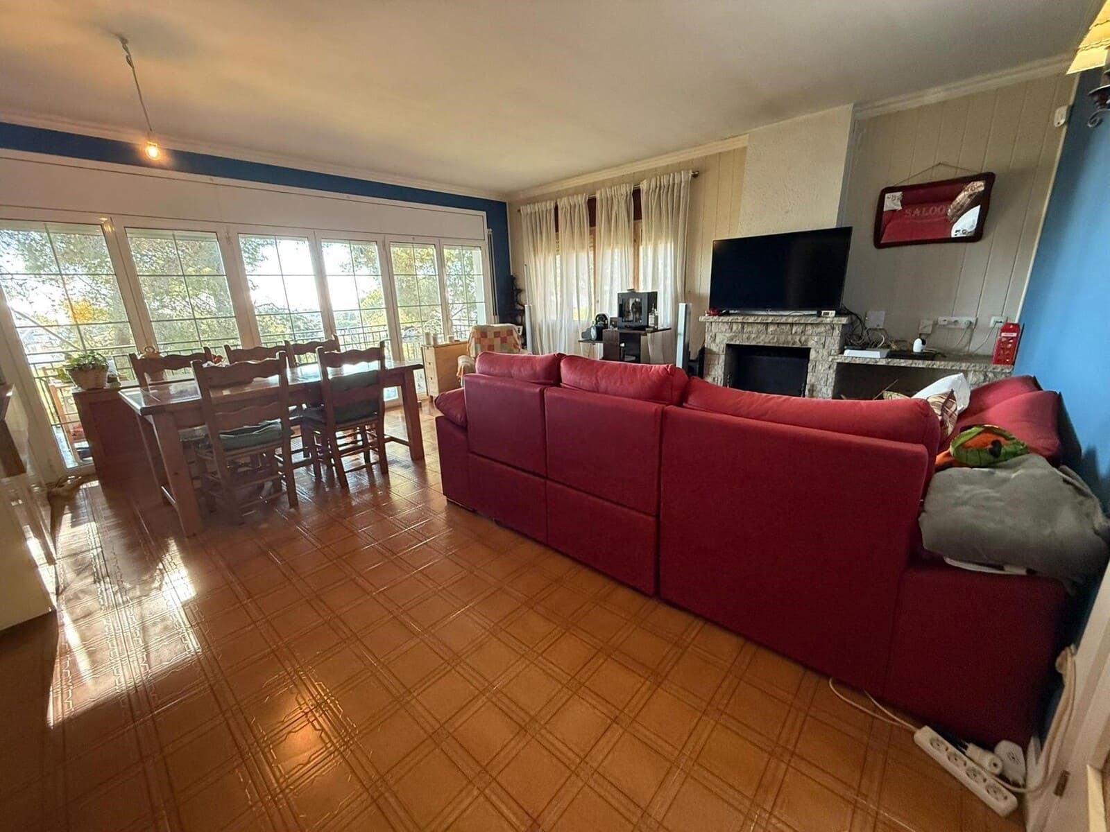 Sala de estar con sofá rojo, mesa de comedor, chimenea y grandes ventanales.