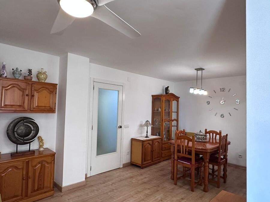 Comedor: muebles de madera, mesa con sillas, reloj, puerta y ventilador de techo.