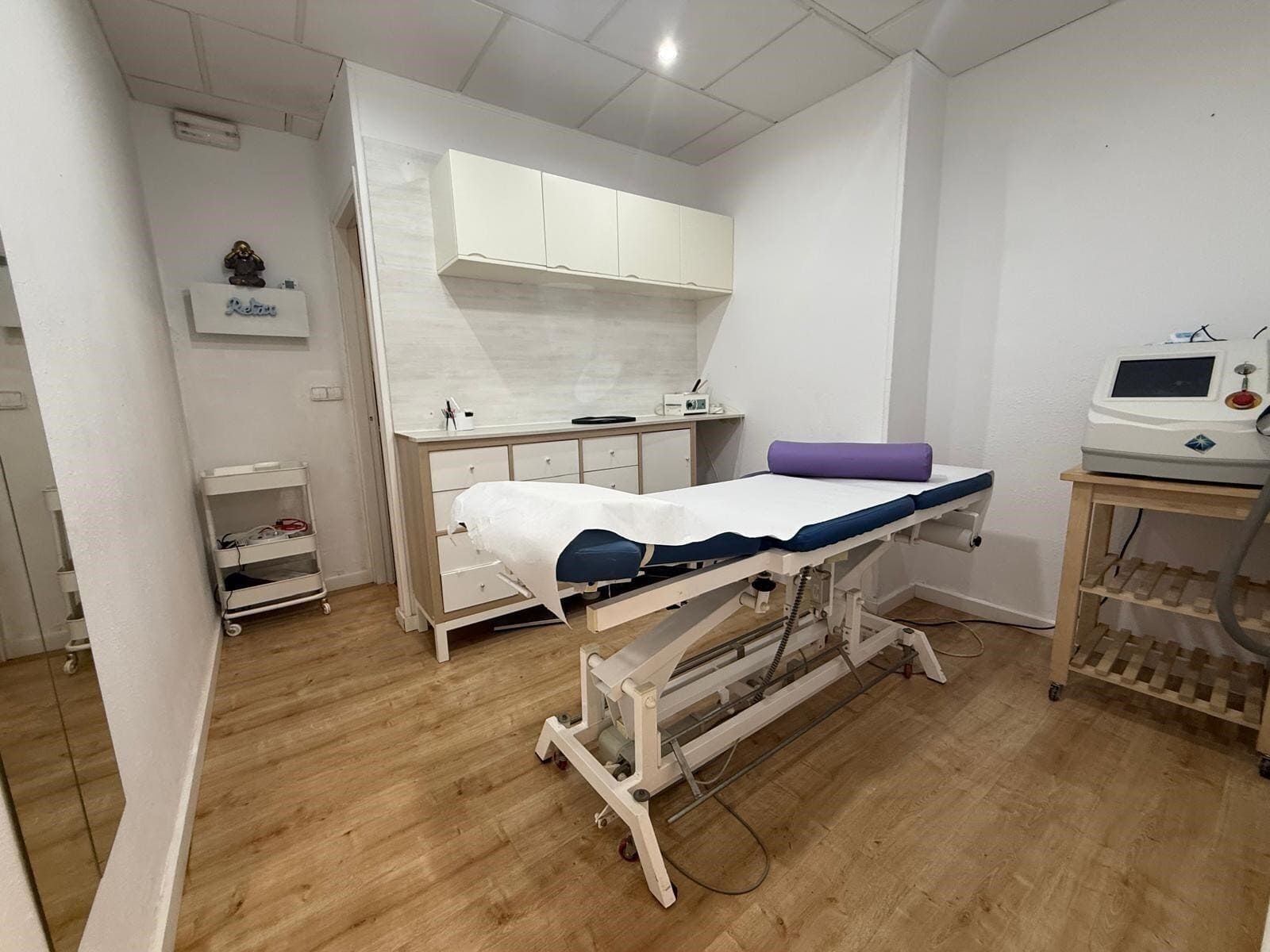 Sala de tratamiento con gabinetes blancos, mesa de exploración y equipo médico.