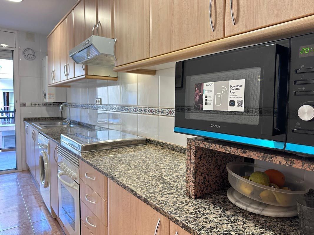 Cocina con gabinetes de madera clara, encimeras de granito, microondas y frutero.