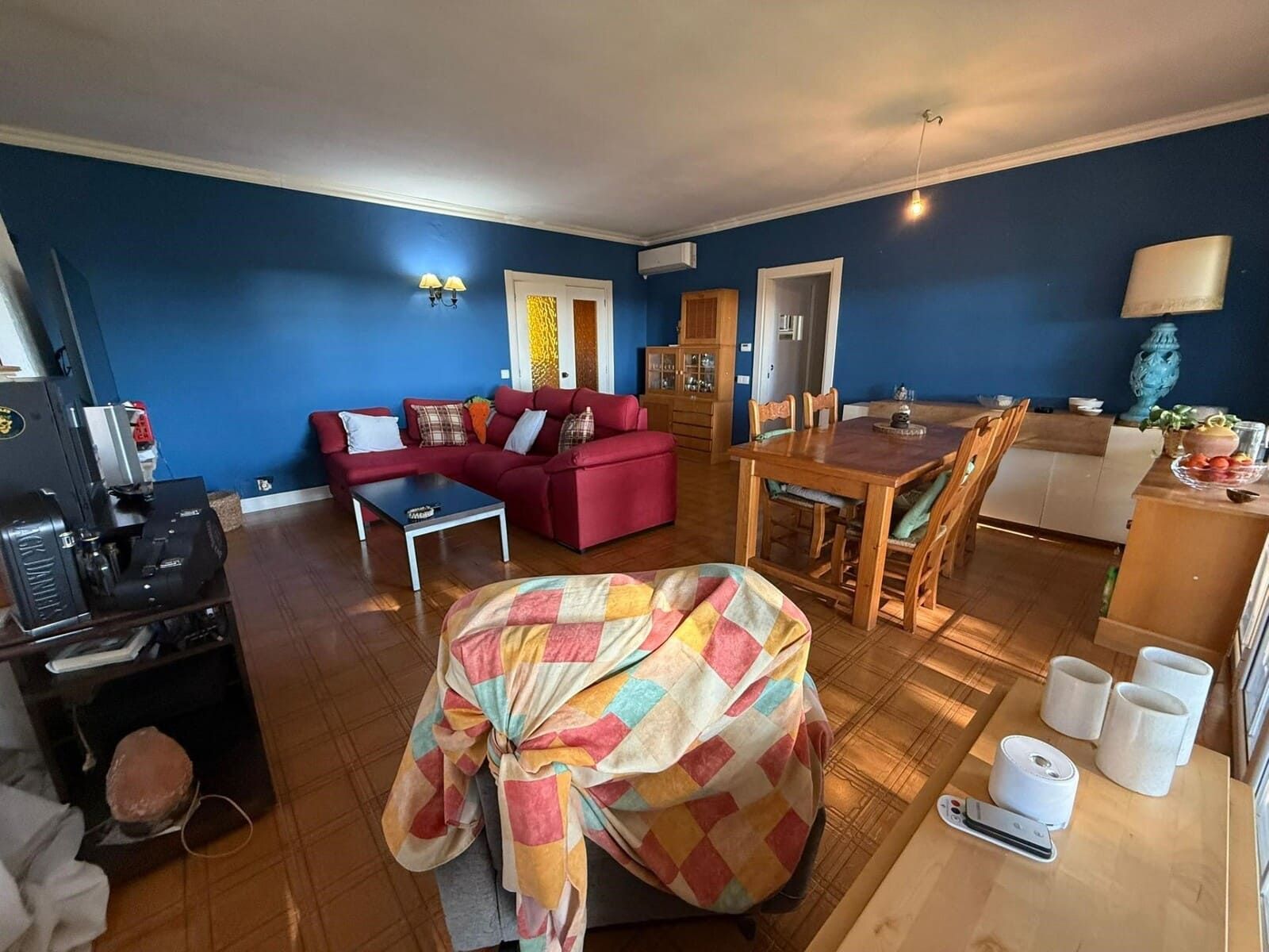 Sala de estar con sofá rojo, paredes azules, muebles de madera y manta estampada.