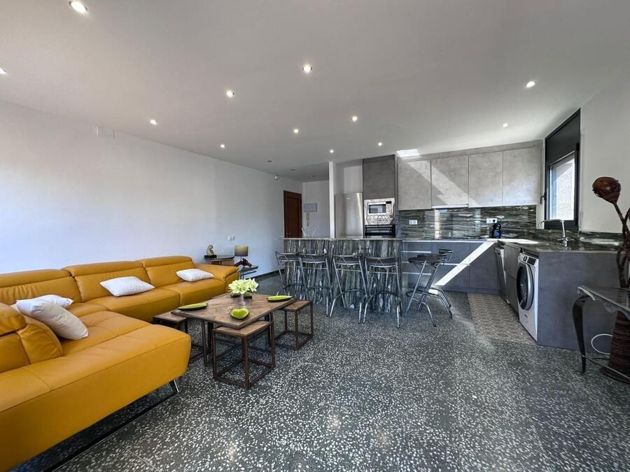Sala de estar de concepto abierto con sofá amarillo, cocina moderna y piso moteado gris.