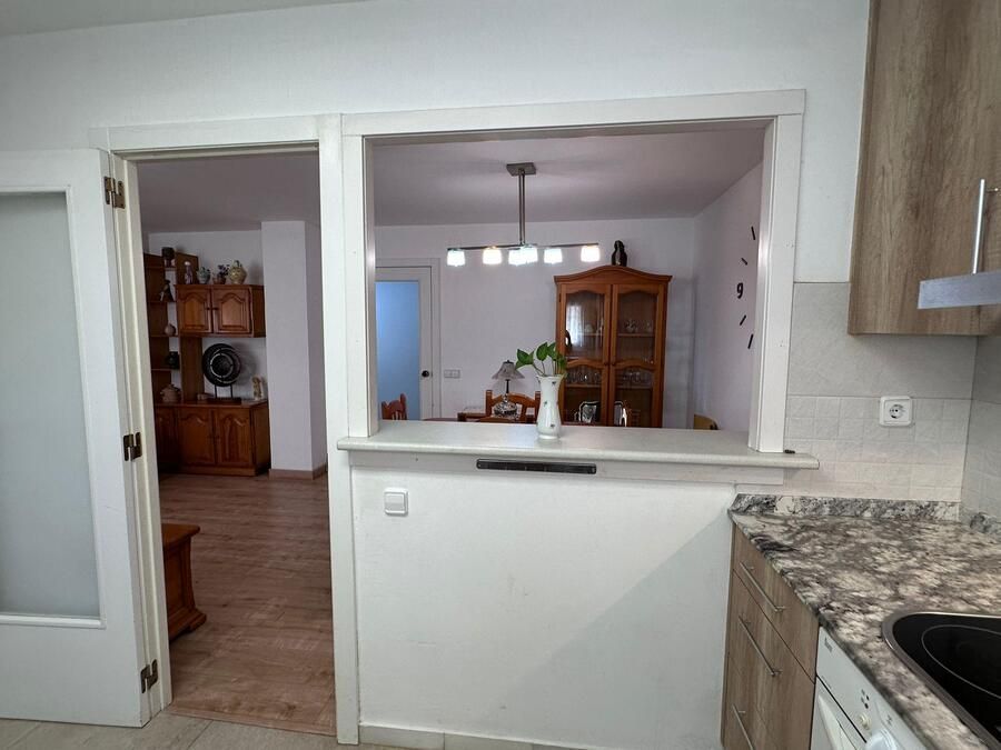 Cocina con acceso directo al comedor. Paredes, encimera y molduras blancas. Armarios y muebles de comedor de madera.