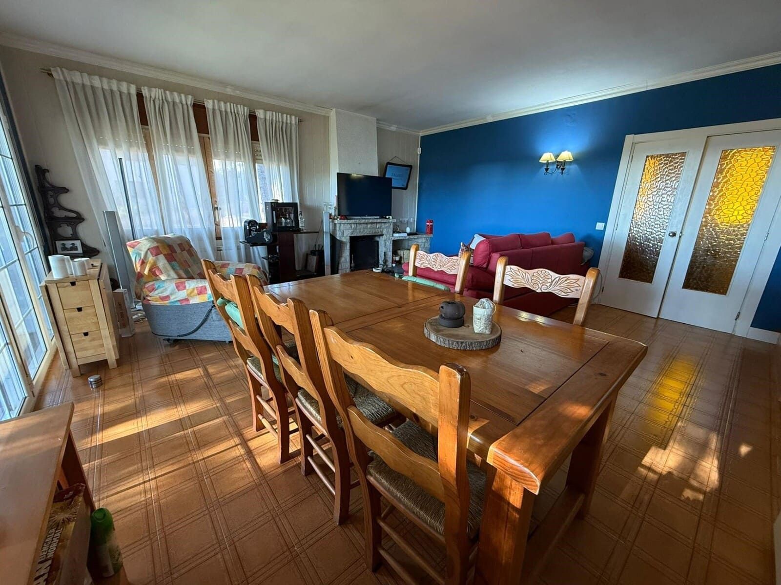 Comedor con mesa y sillas de madera, luz solar, pared de acento azul, chimenea y sofá.