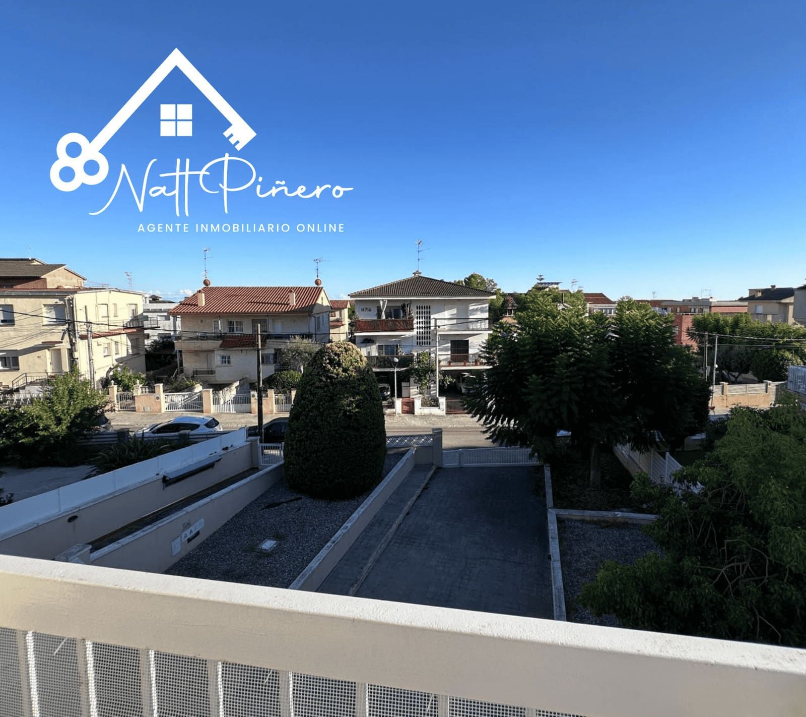 Vista desde un balcón con vista a una calle con edificios, árboles y cielo azul.