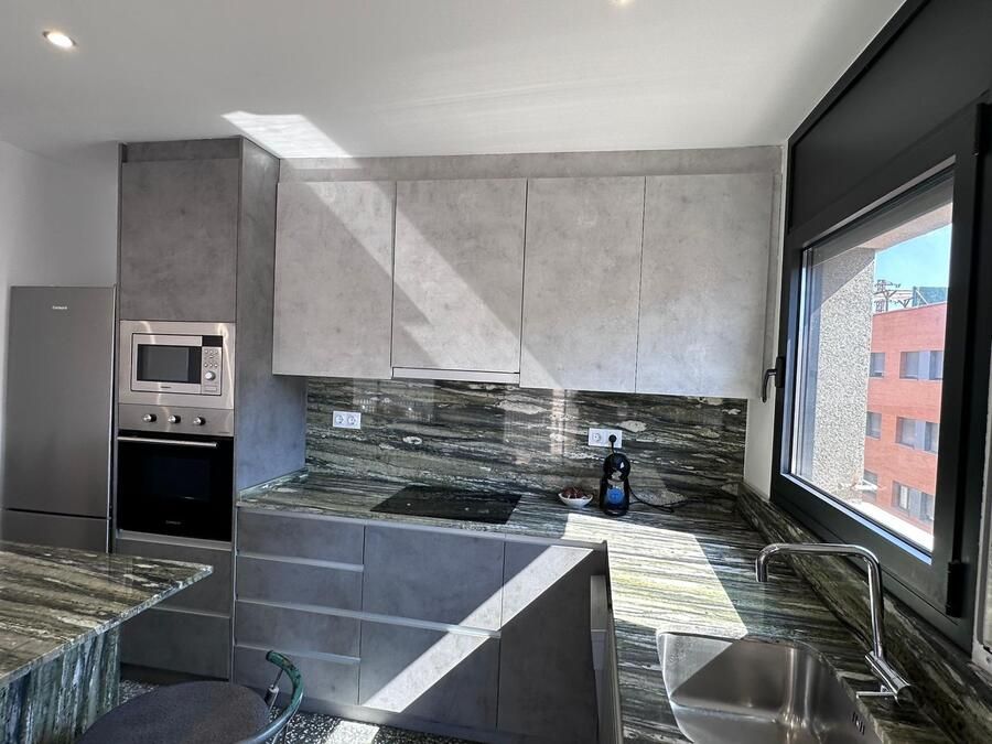 Cocina moderna con gabinetes grises, encimeras de granito y electrodomésticos de acero inoxidable.