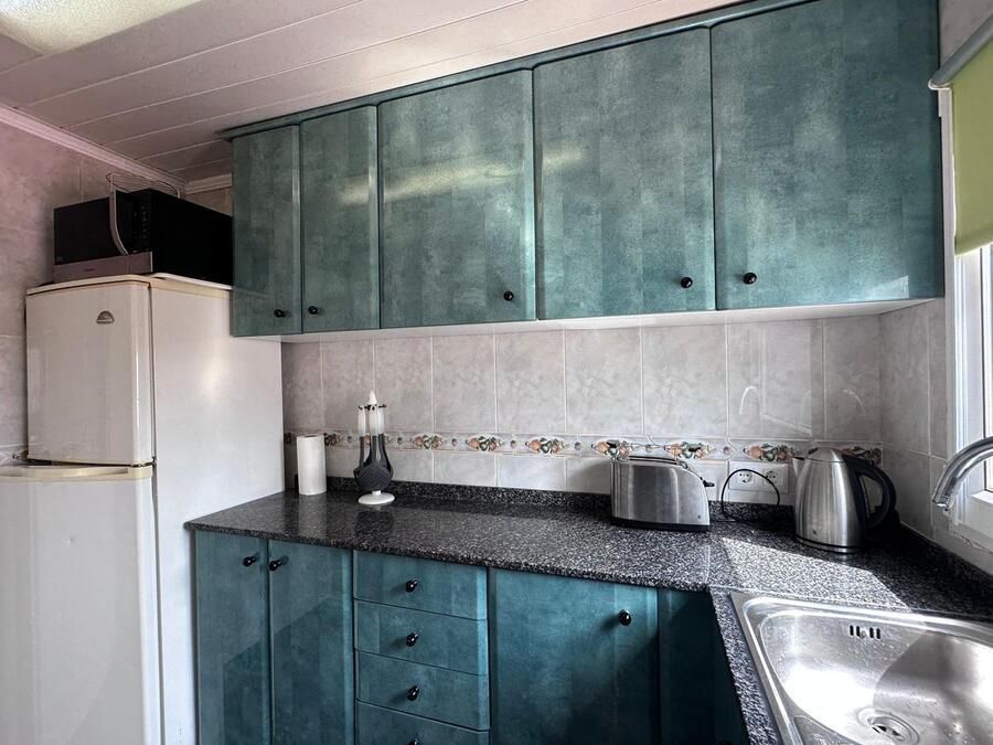 Cocina con gabinetes color verde azulado, encimera negra y fregadero de acero inoxidable.