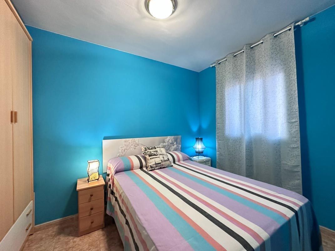 Dormitorio con paredes turquesas, colcha de rayas y mesita de noche con lámpara.