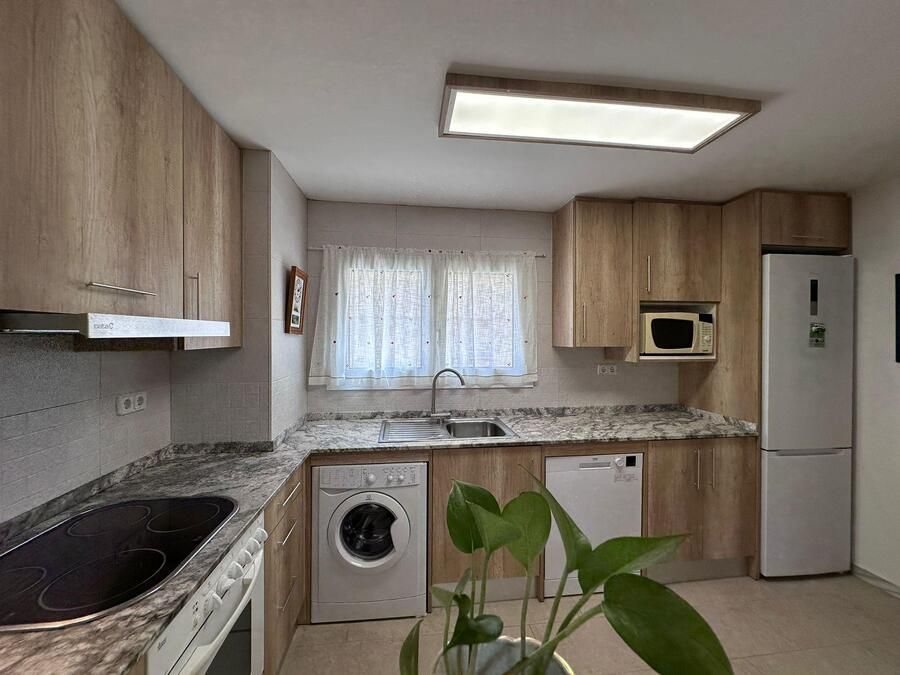 Cocina con gabinetes de madera clara, encimeras de granito y electrodomésticos como microondas y refrigerador.
