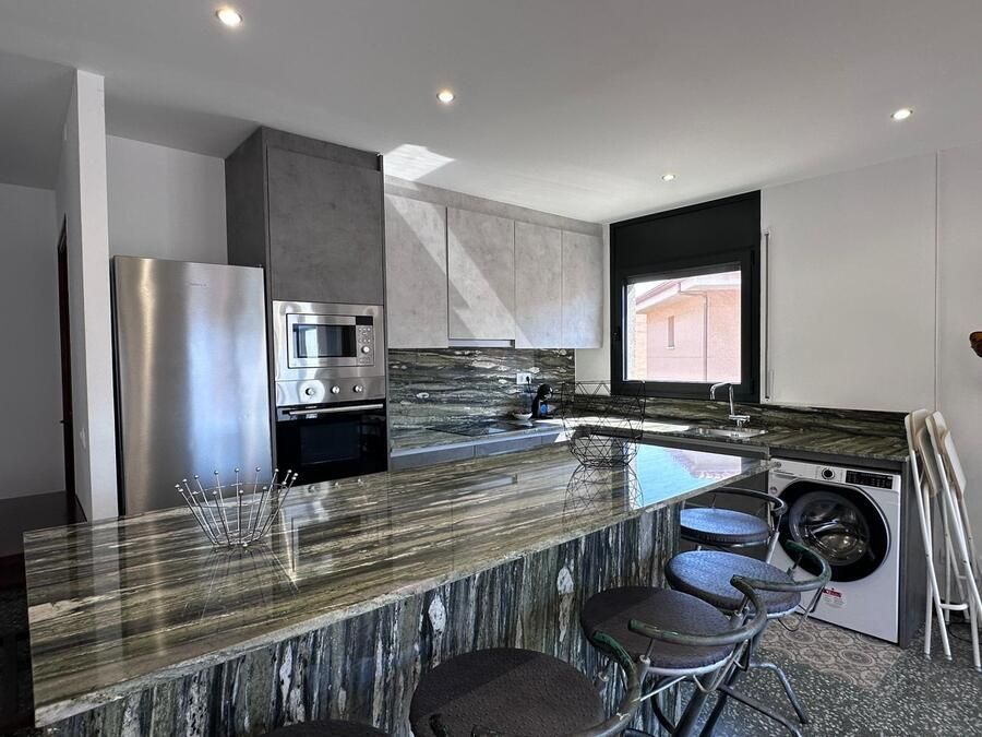 Cocina moderna con encimeras de granito, electrodomésticos de acero inoxidable y taburetes de bar.