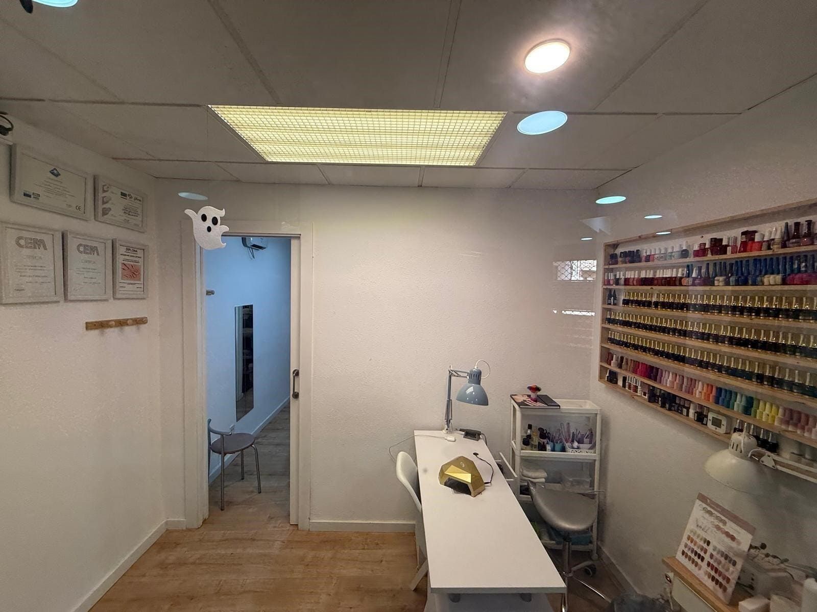 Interior de salón de uñas con exhibición de esmaltes de uñas, estación de trabajo y puerta.