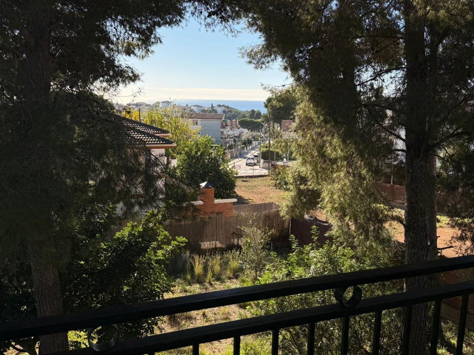 Vista desde un balcón con vistas a una ciudad, árboles y el mar en un día soleado.
