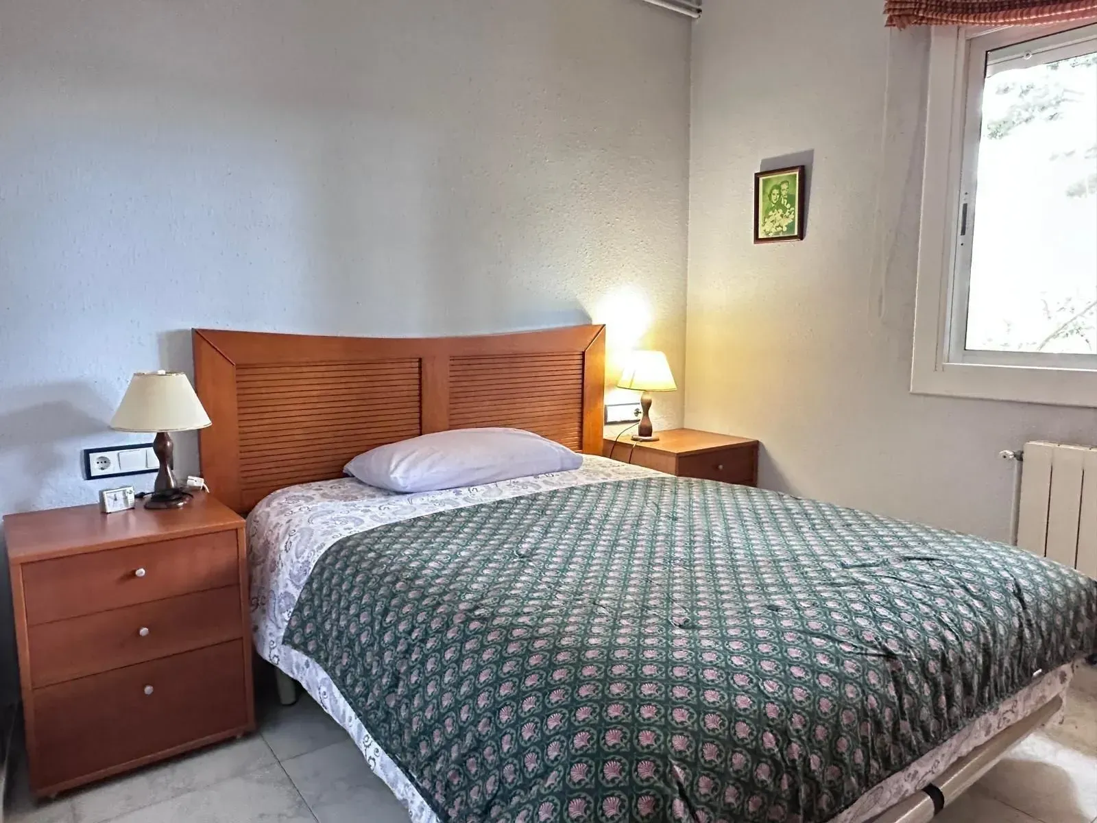 Un dormitorio con una cama, dos mesitas de noche, dos lámparas y una ventana.