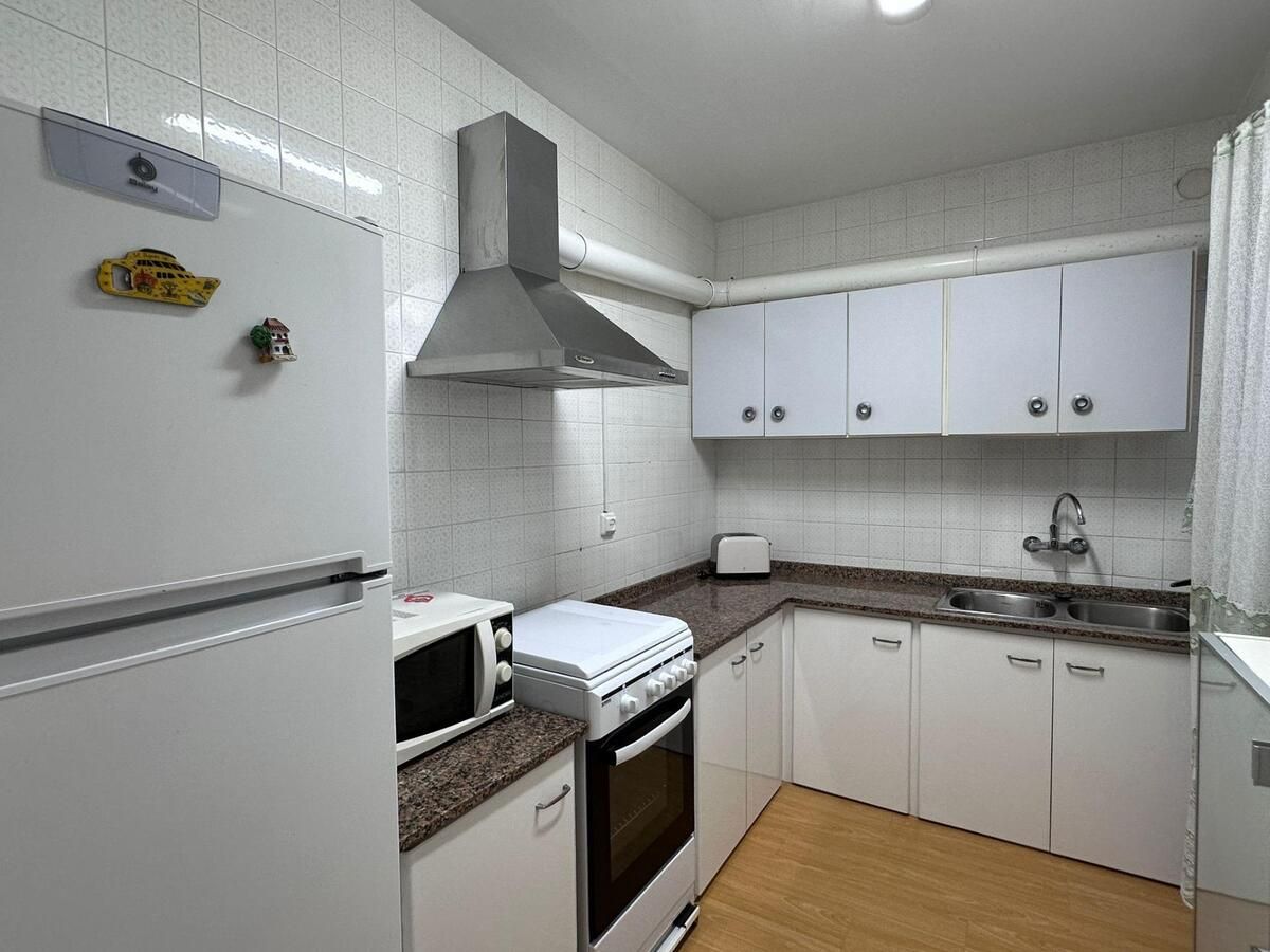 Cocina pequeña y blanca con electrodomésticos y gabinetes, piso de madera y paredes de azulejos.