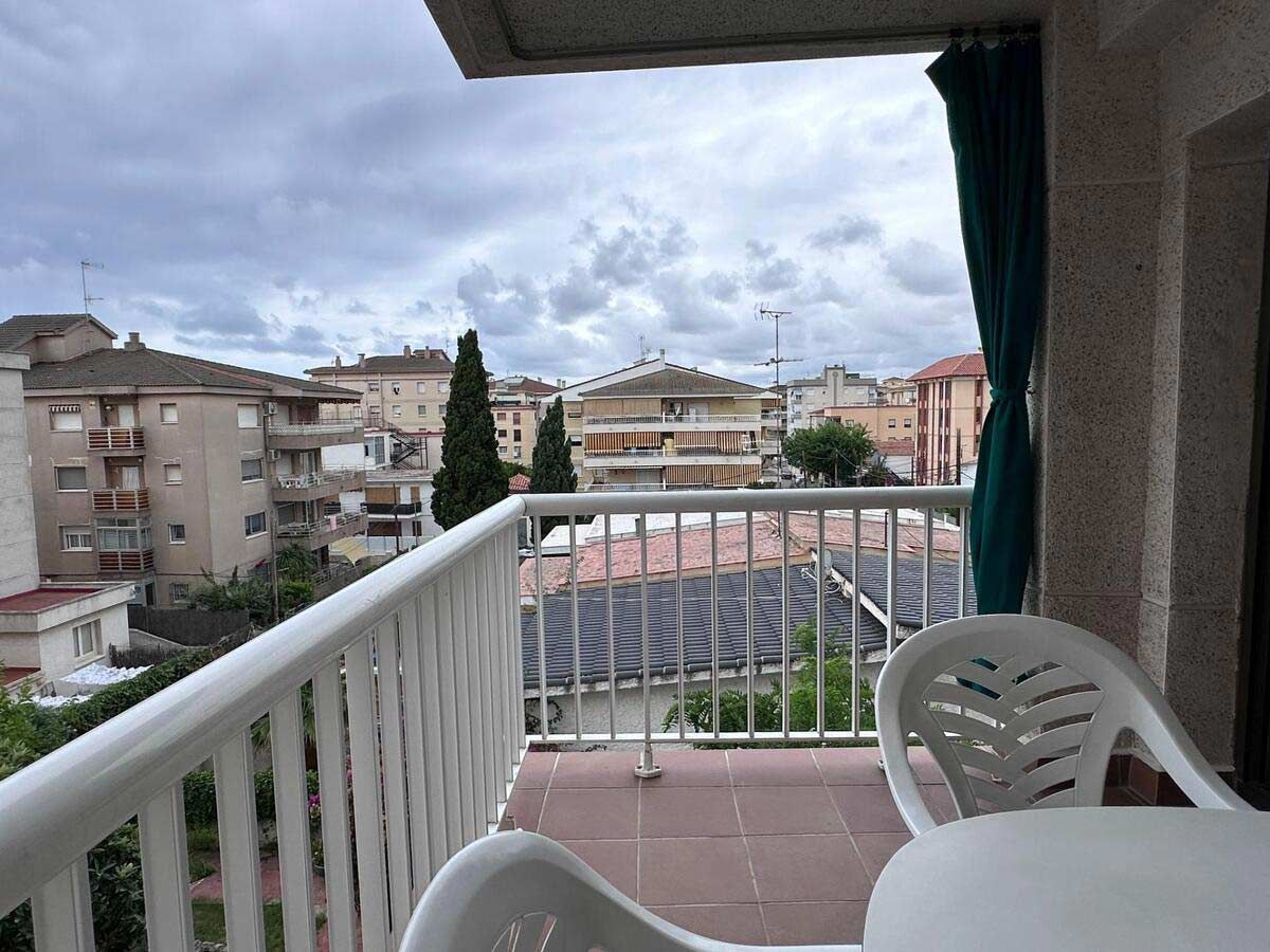 Balcón con vista a un pueblo, con barandilla blanca, dos sillas blancas y un cielo nublado.