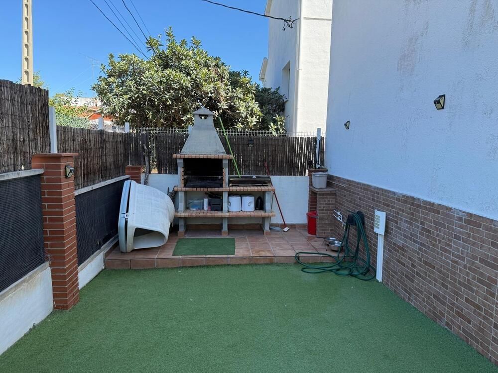 Espacio exterior con parrilla, césped artificial, cerco de madera y casa blanca.