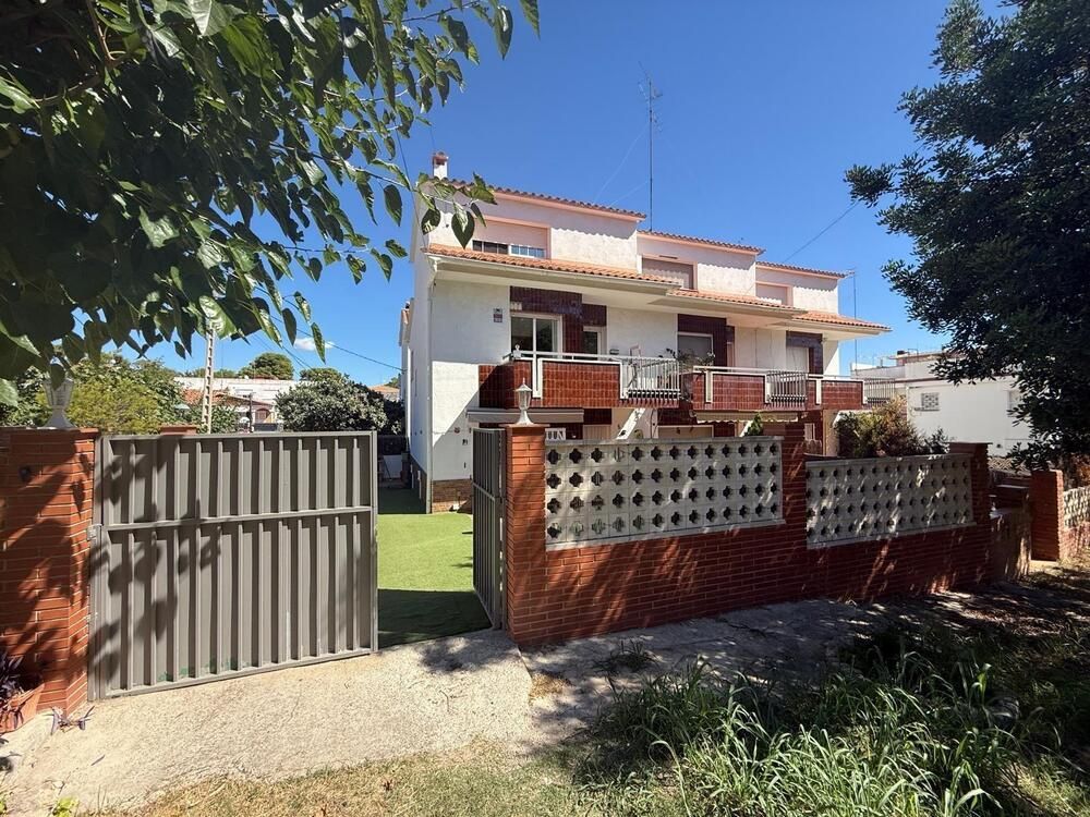 Casa blanca de dos pisos con cerca de ladrillo, césped verde y puerta gris abierta bajo un cielo azul.