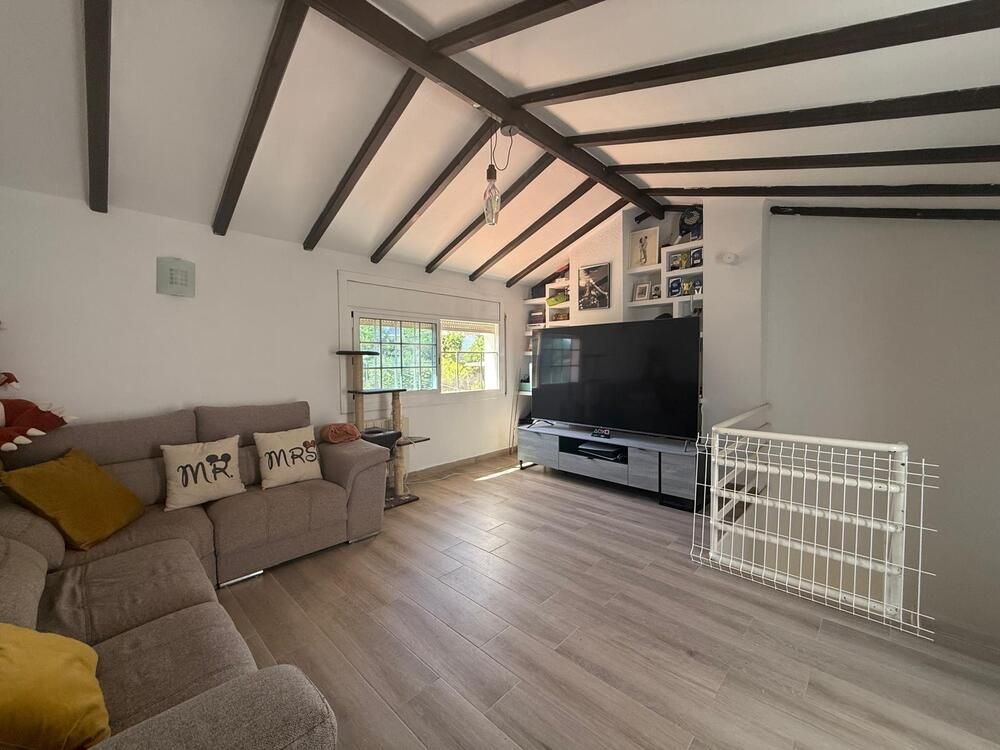 Sala de estar con sofá seccional gris, TV y fotografías enmarcadas bajo un techo con vigas de madera.