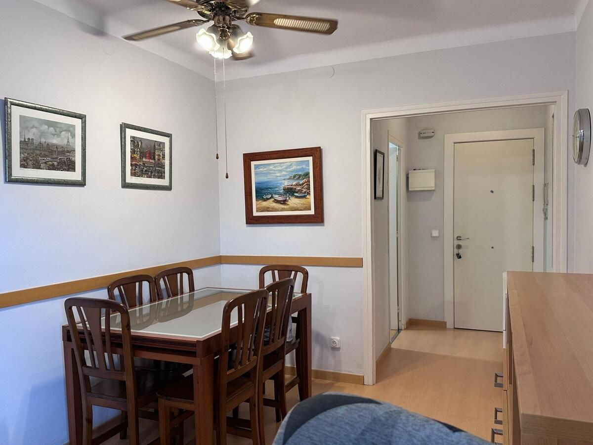 Comedor con mesa y sillas de madera, obras de arte y puerta abierta a un pasillo.