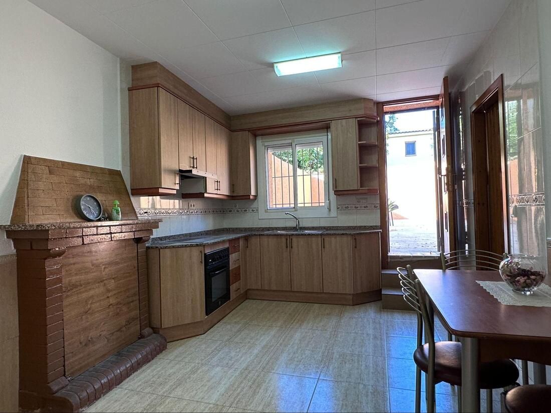 Cocina con armarios de madera, encimeras de piedra, ventana, puerta y mesa.