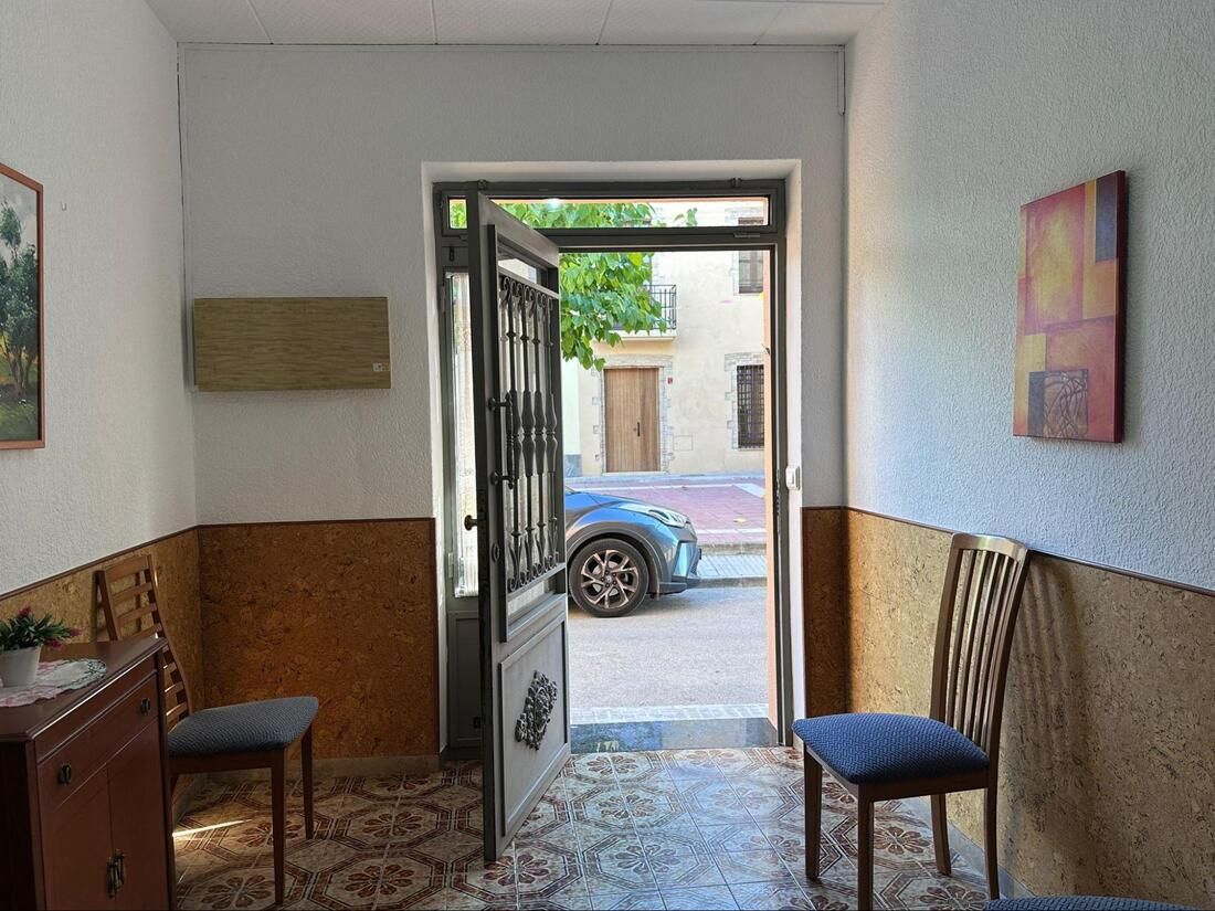 La puerta interior da a la calle. Dos sillas flanquean la entrada. Paredes marrones, beige y blancas.