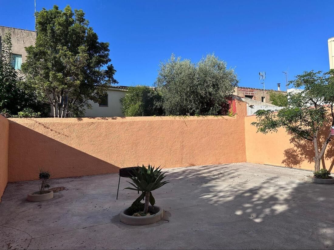 Pared de estuco naranja con árboles y sombras, recortada contra un cielo azul brillante.