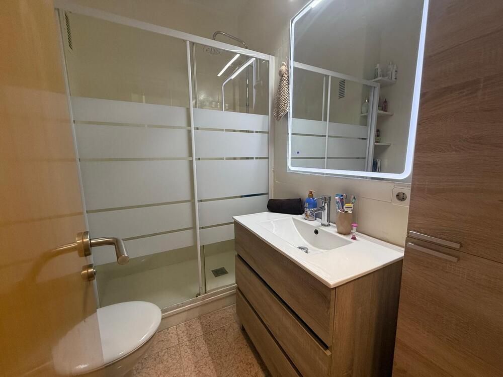 Baño con ducha de cristal, tocador de madera y espejo iluminado.