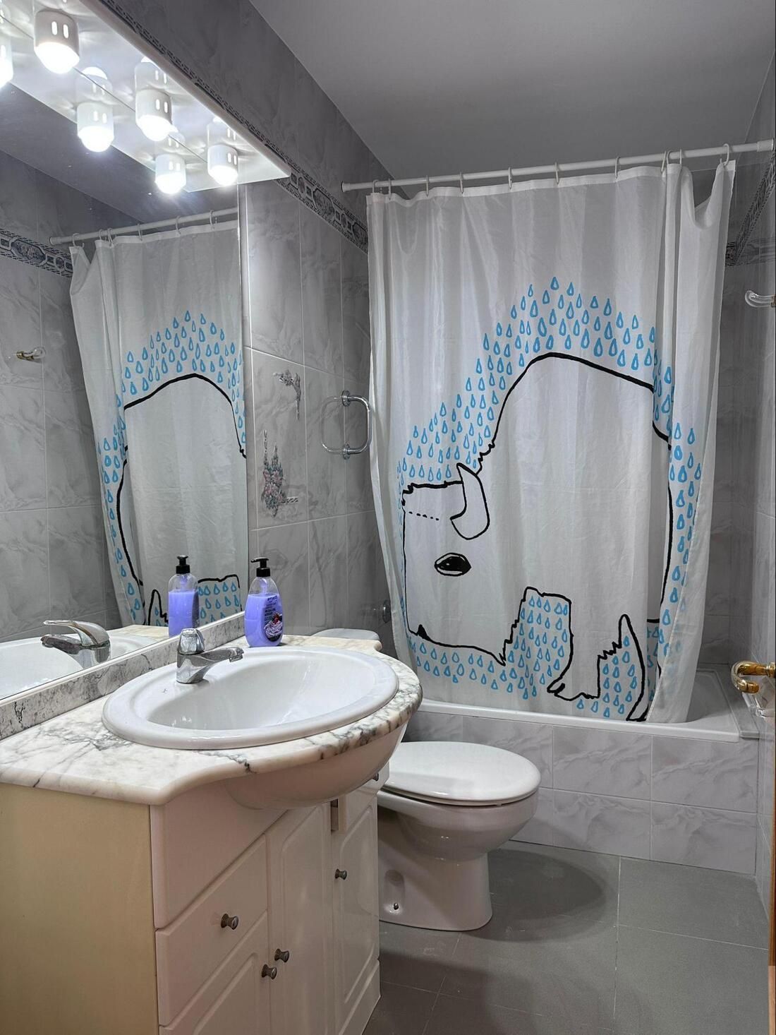 Baño con lavabo, inodoro y bañera blancos. La cortina de la ducha tiene un diseño de animal azul.