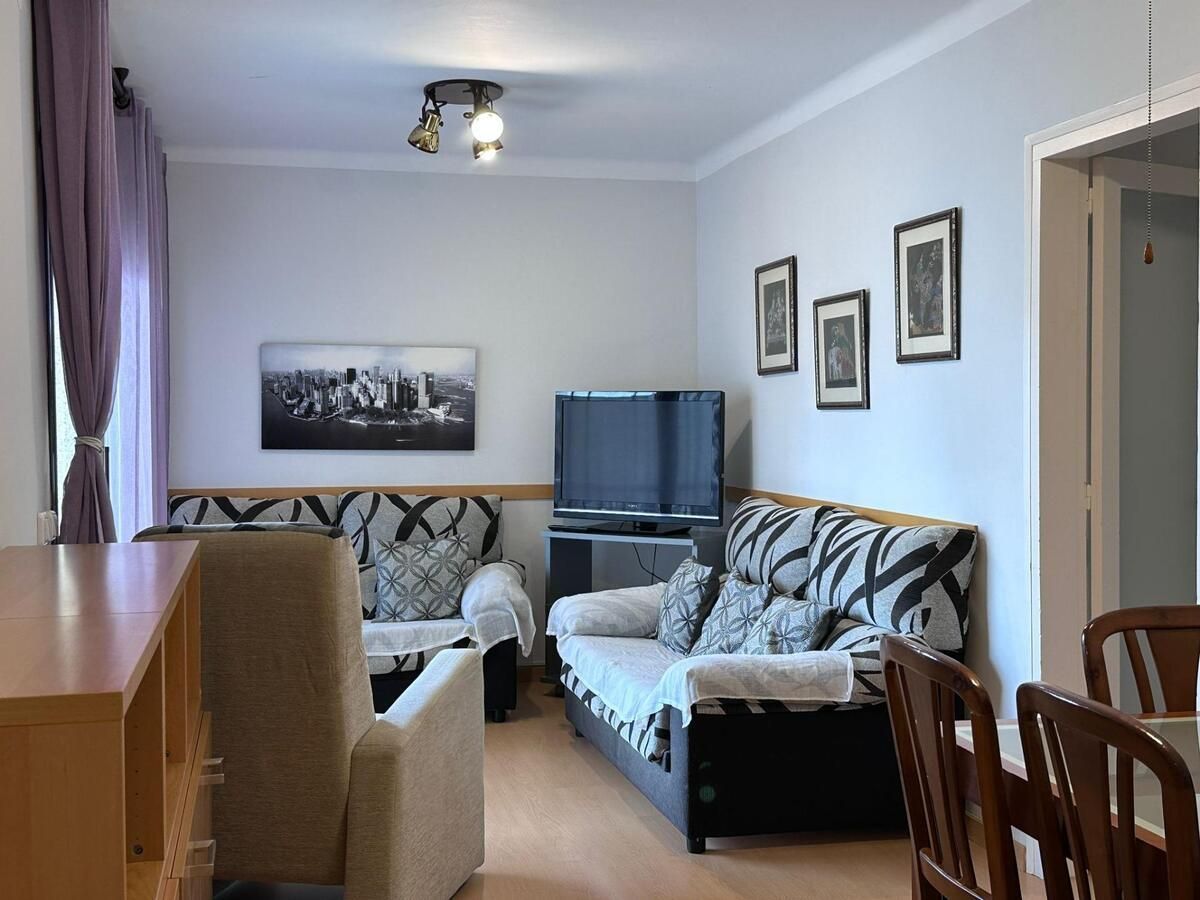 Sala de estar con dos sofás estampados, TV, obras de arte y comedor visibles.