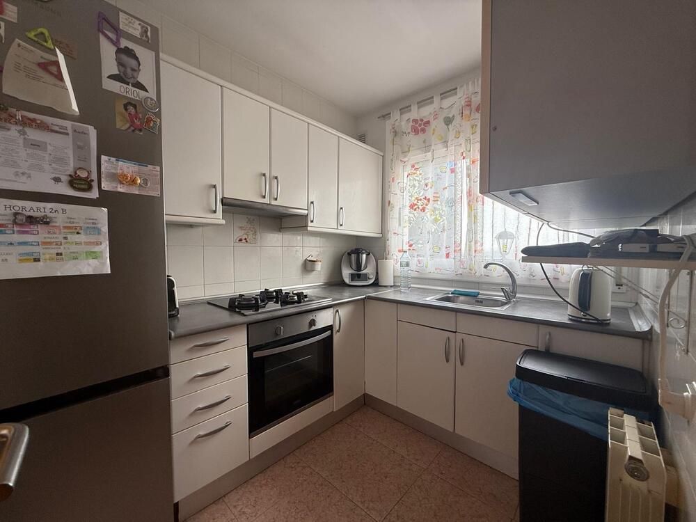 Cocina pequeña con gabinetes blancos, electrodomésticos y una ventana con cortina floral.