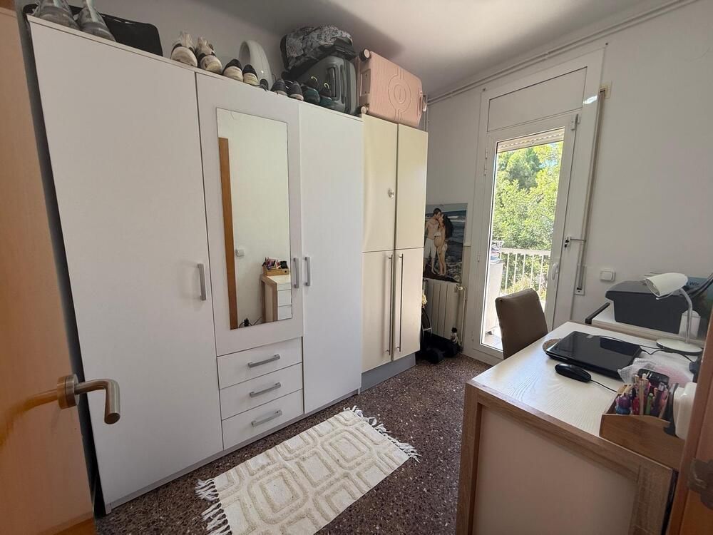 Armarios blancos llenan una habitación, cerca de una ventana y un escritorio. Una alfombra yace sobre el suelo moteado.