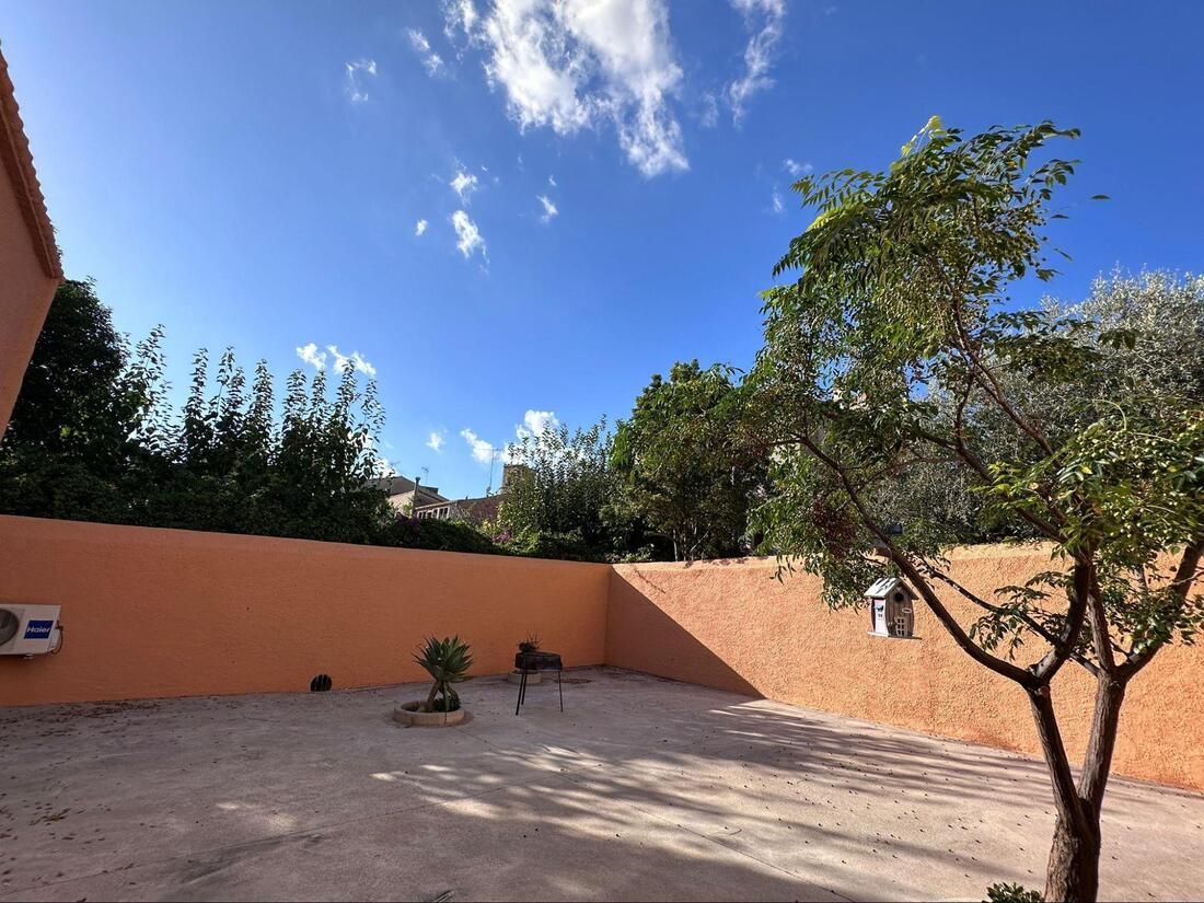 Un espacio exterior soleado con una pared naranja, árboles y cielo azul.