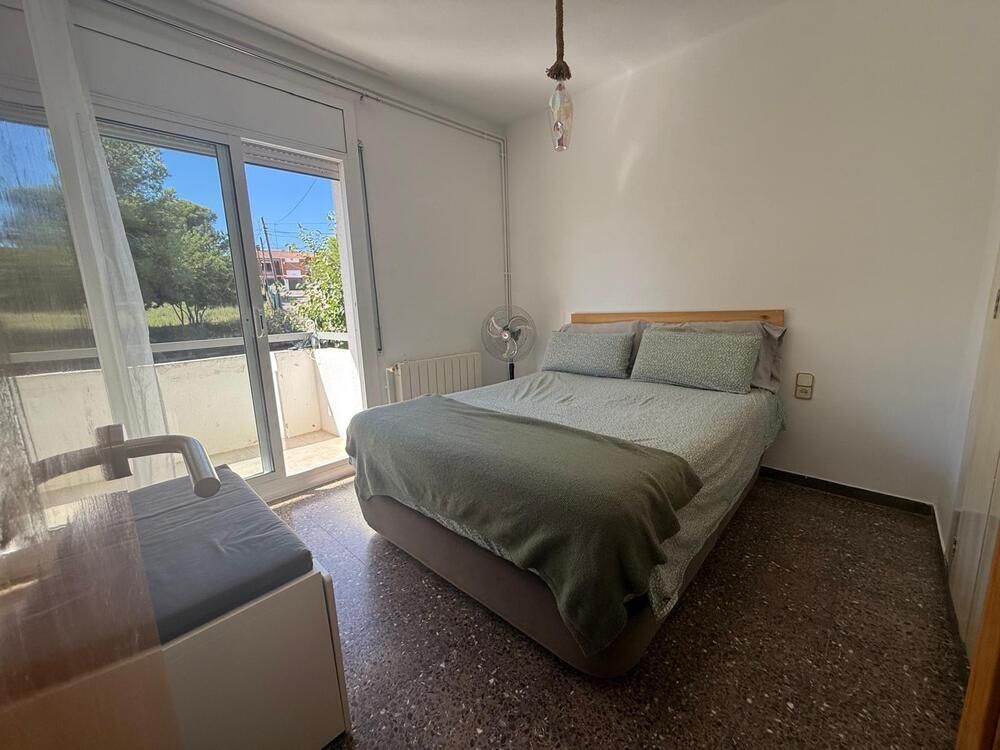 Dormitorio con cama, balcón, paredes blancas y suelo de terrazo.